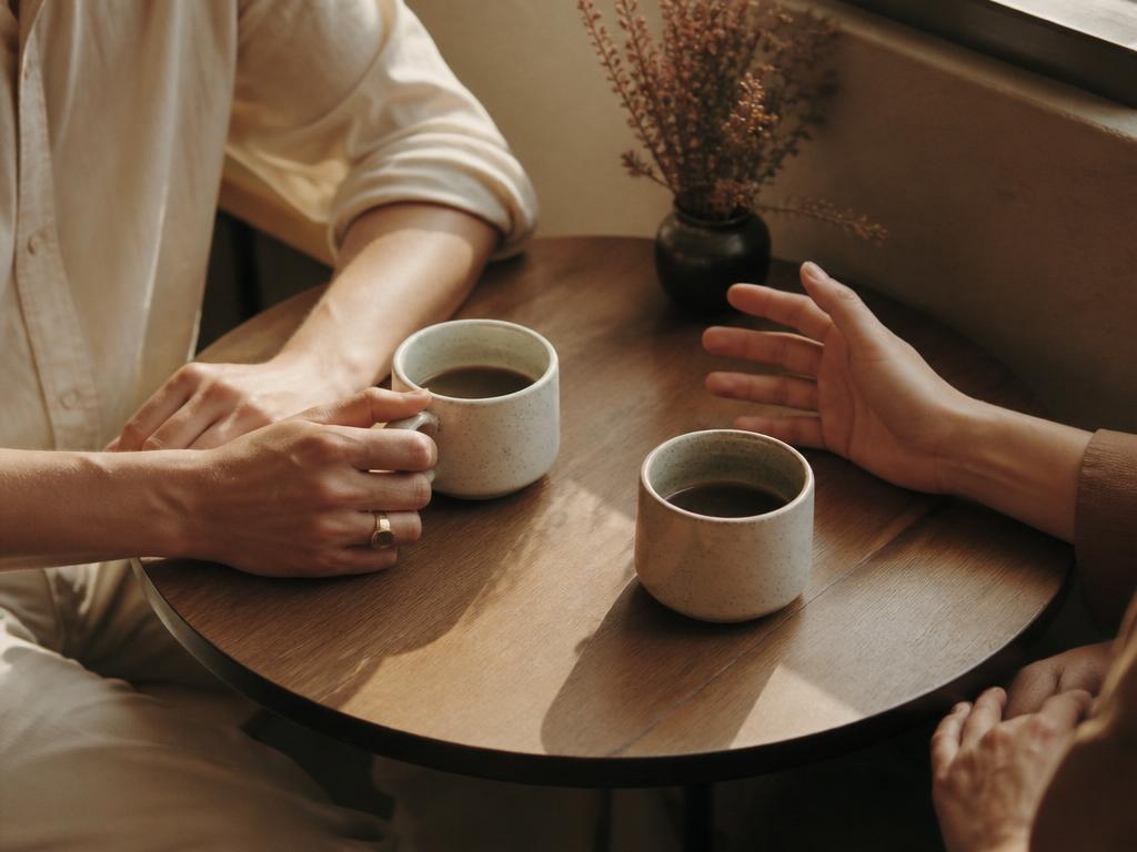 Two coffee cups and two pairs of hands on a café table, mid-conversation