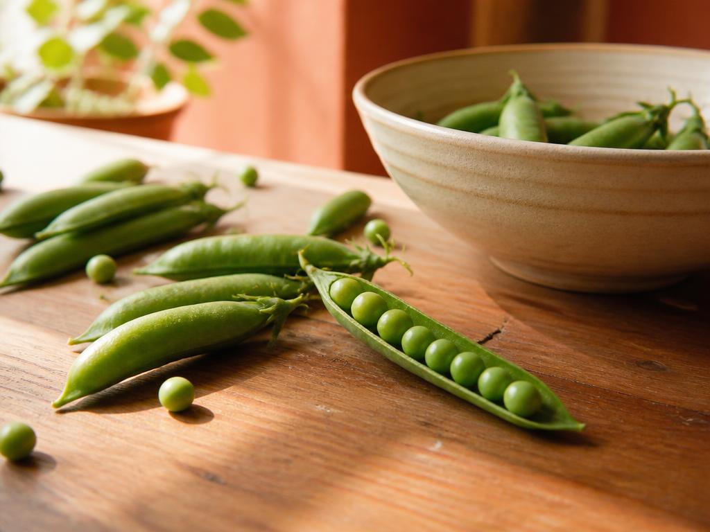 Fresh pea pods on a kitchen table, one split open to show a neat row of peas